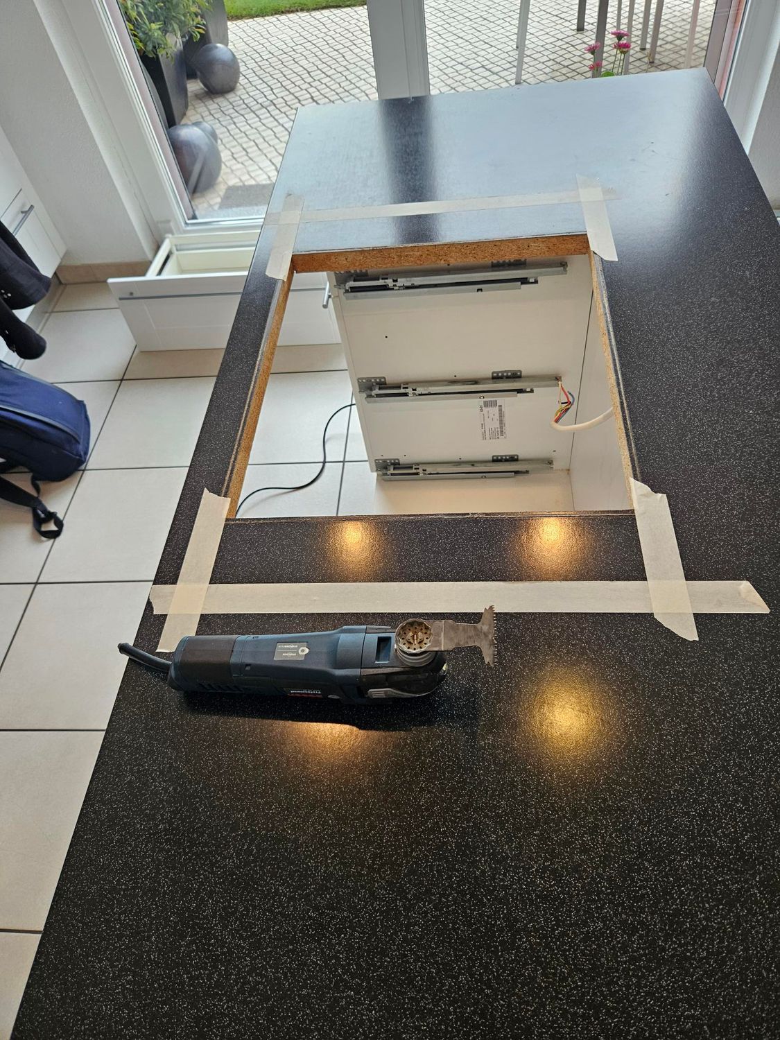 Découpe du plan de travail de la cuisine pour l'installation d'un tiroir. Un outil est posé sur le plan de travail près de la découpe.