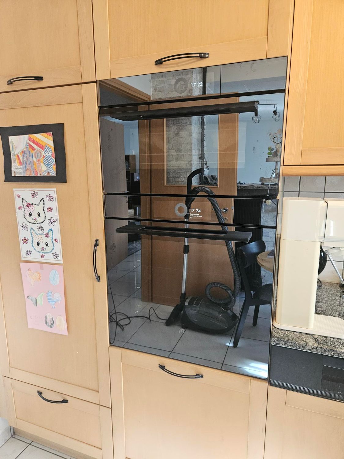 Four encastré dans les placards de cuisine, avec un aspirateur et d'autres éléments visibles à travers la porte vitrée.