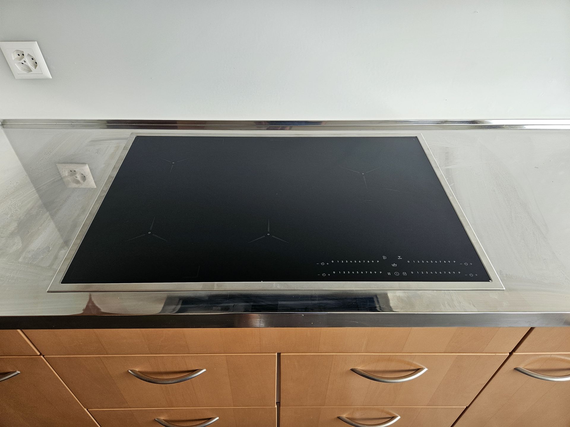 Plaque de cuisson à induction noire encastrée dans un cadre en acier inoxydable au-dessus de placards en bois clair.