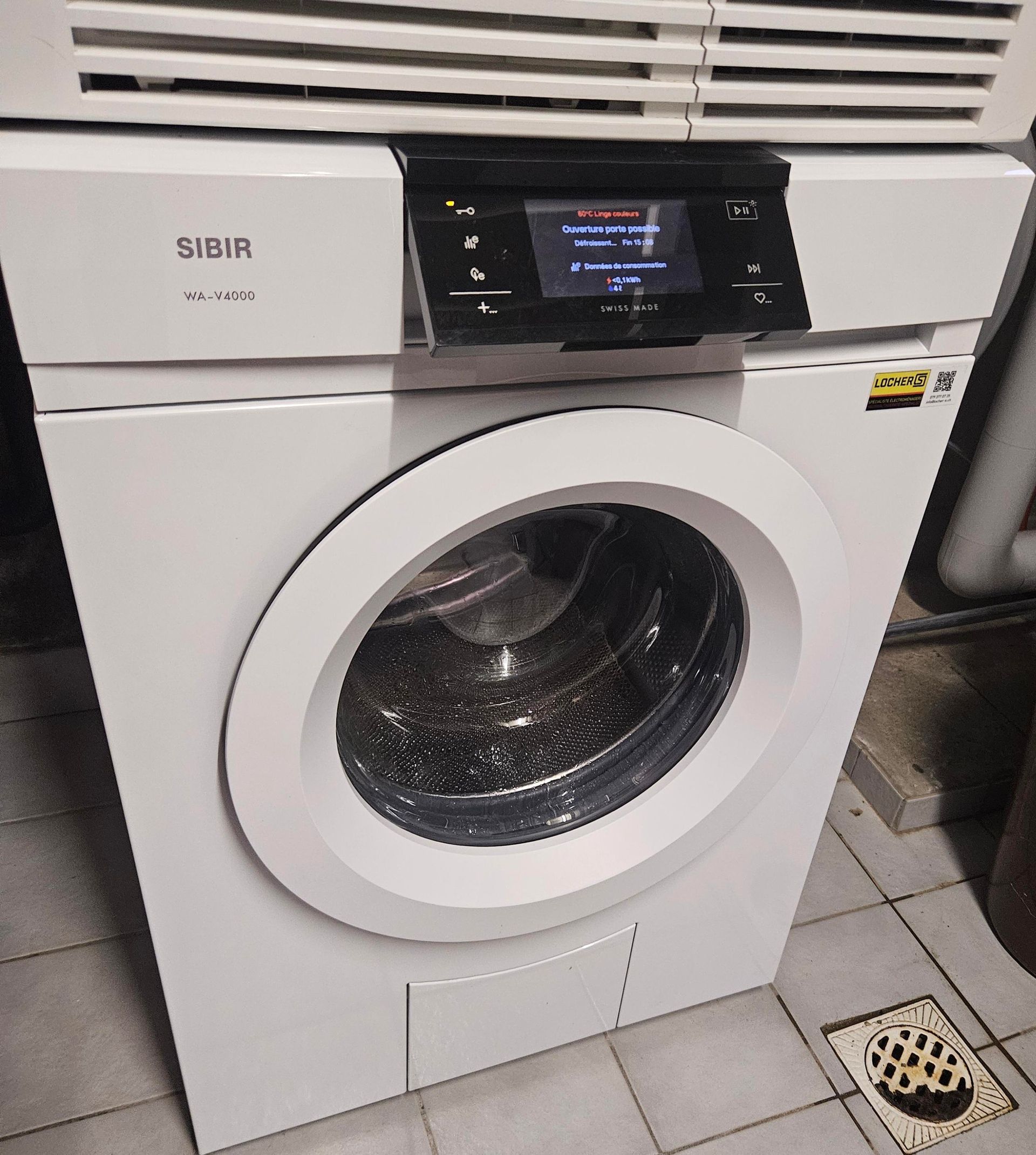 Machine à laver blanche avec panneau de commande numérique ; installée au sous-sol.