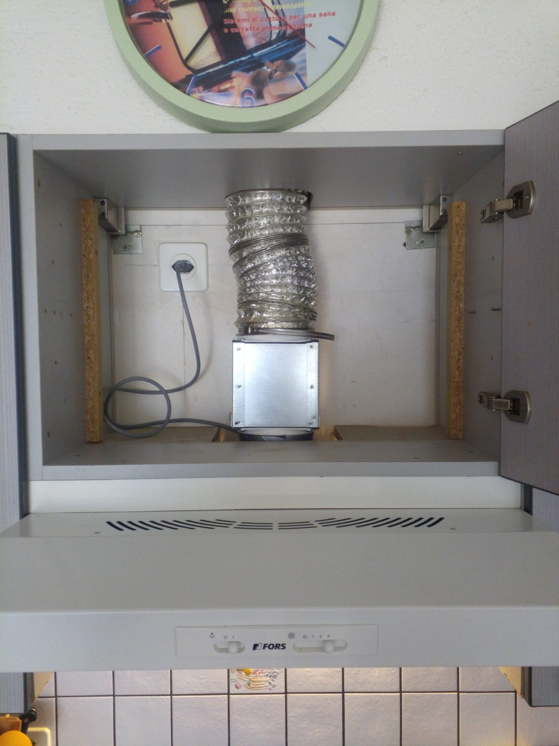 À l'intérieur d'un meuble de cuisine avec hotte aspirante et conduit d'aération, prise électrique et supports de fixation.
