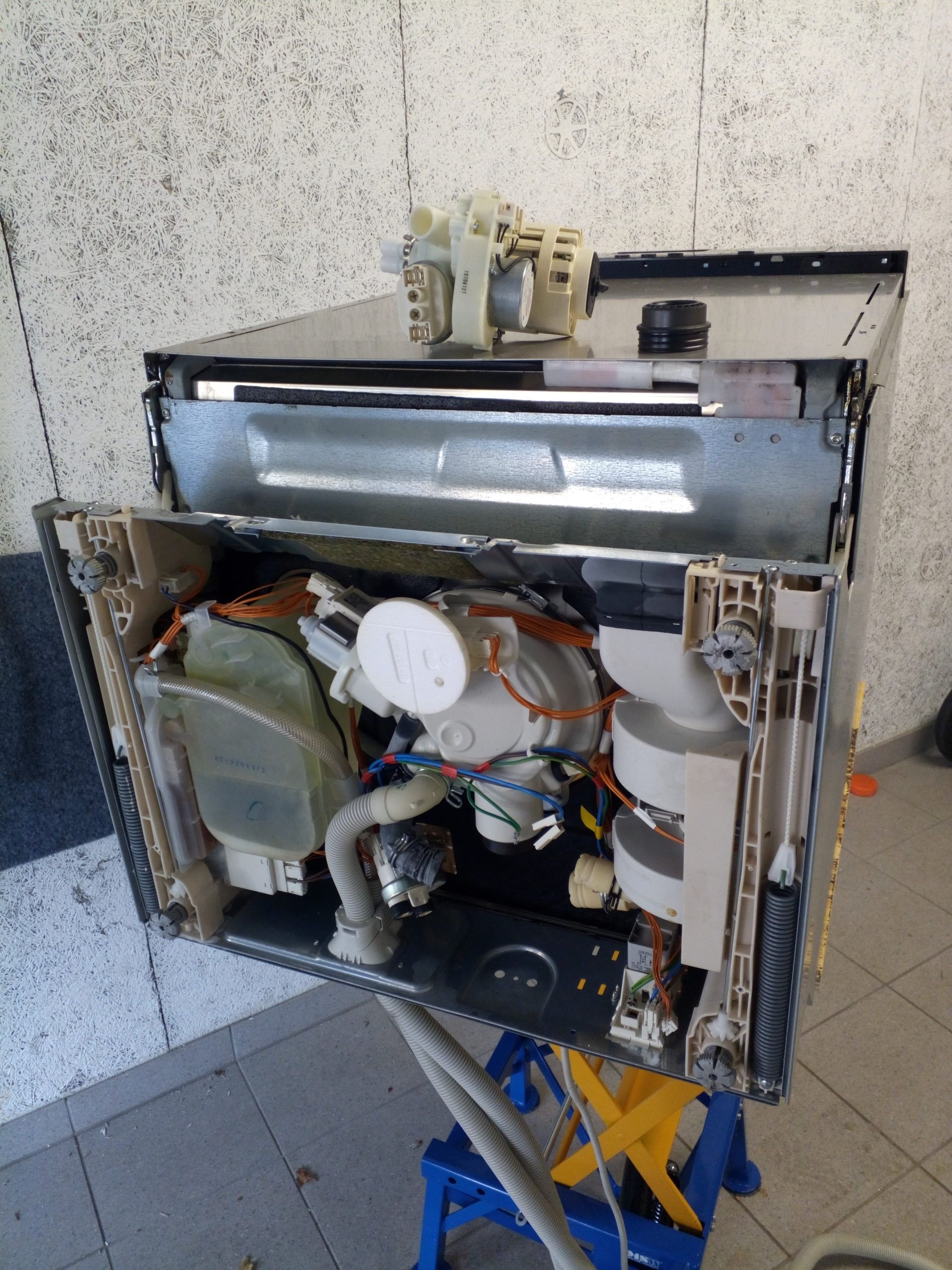 Vue intérieure d'un lave-vaisselle avec le panneau avant ouvert, révélant les composants internes, notamment les pompes et les réservoirs.