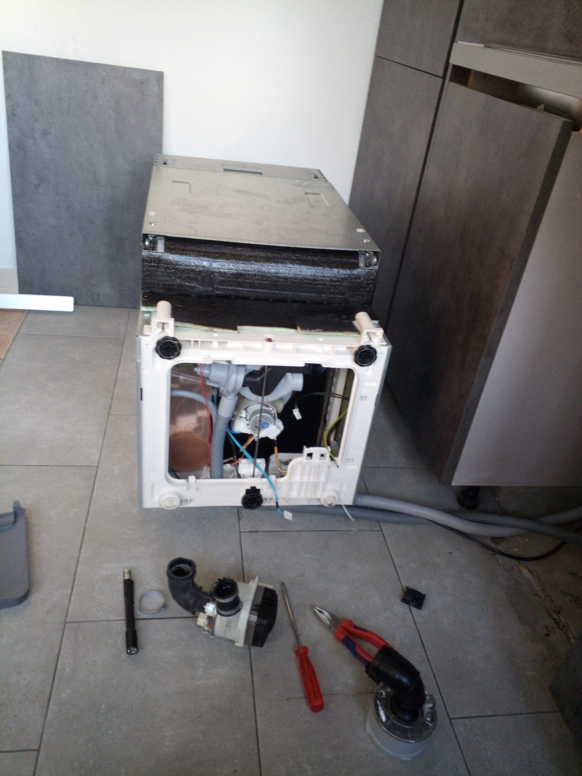 Lave-vaisselle dont le panneau inférieur a été retiré, laissant apparaître les composants internes et la tuyauterie.