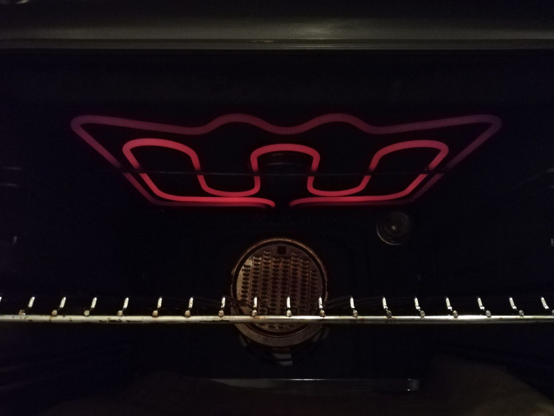 À l'intérieur du four, une résistance rouge illuminée en forme de couronne. Grille et éclairage en dessous.