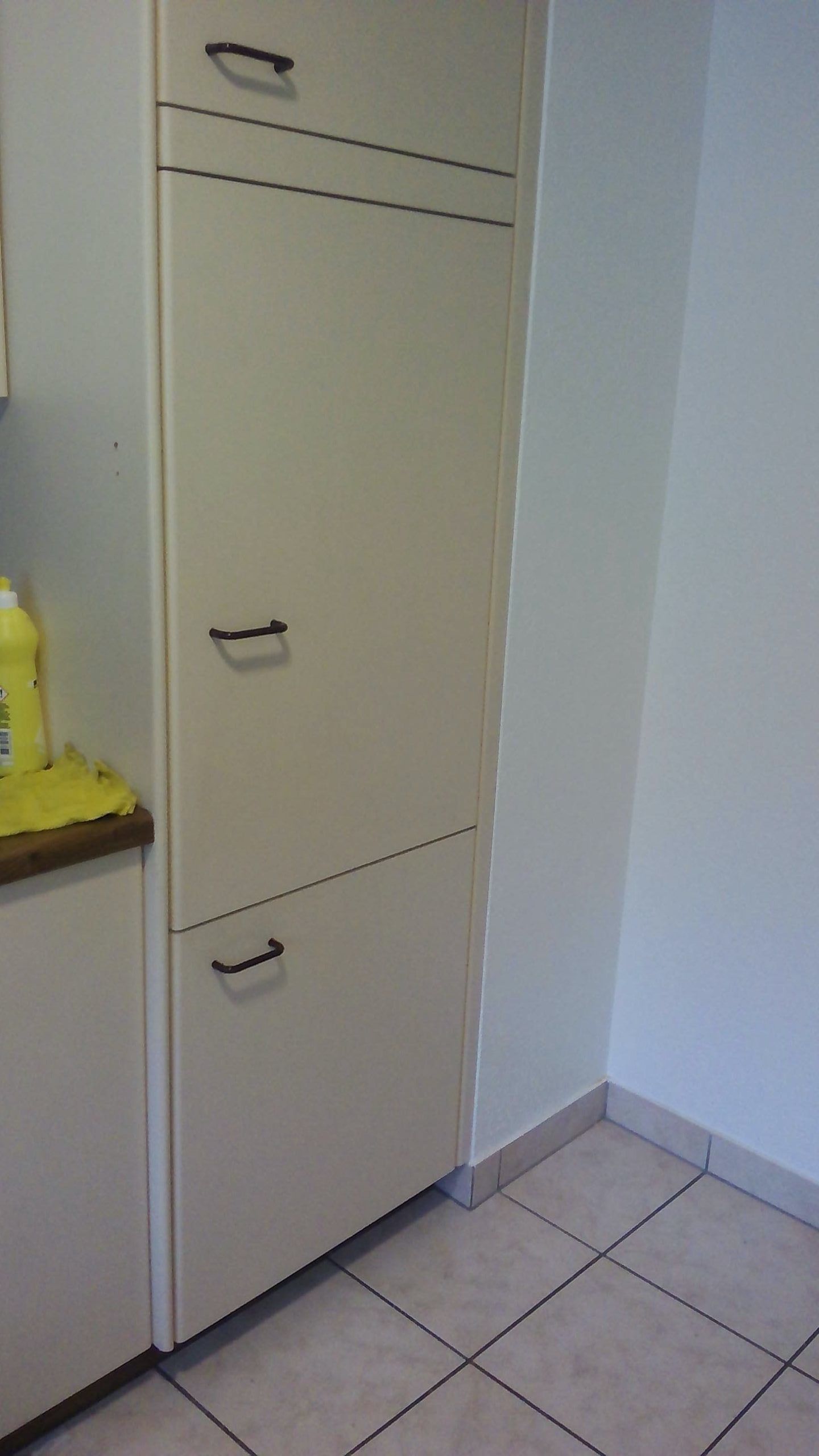 Meuble beige à deux portes et poignées noires, placé contre un mur blanc.