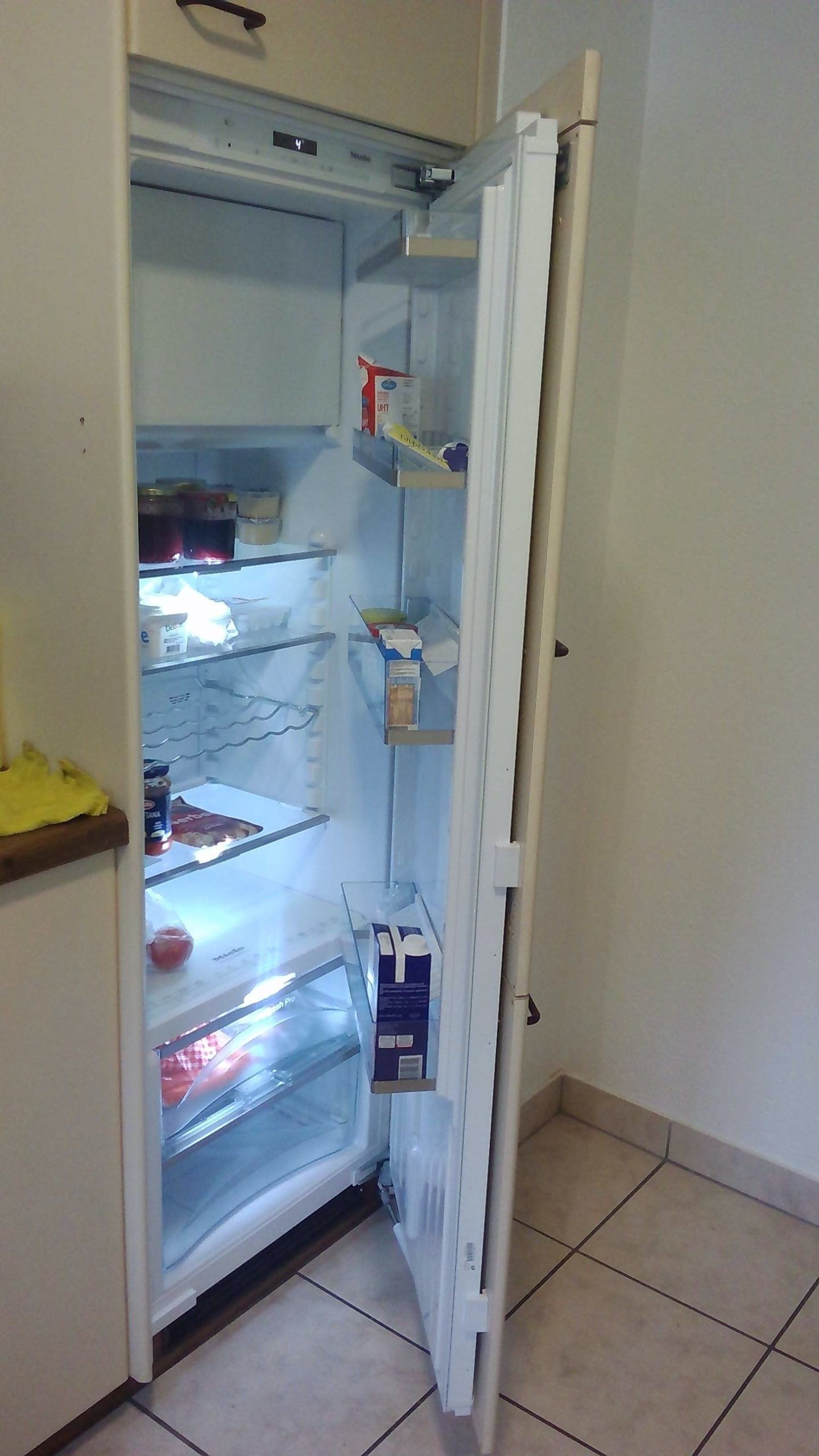 Un réfrigérateur ouvert, presque vide, avec des aliments sur les étagères du haut et du bas.