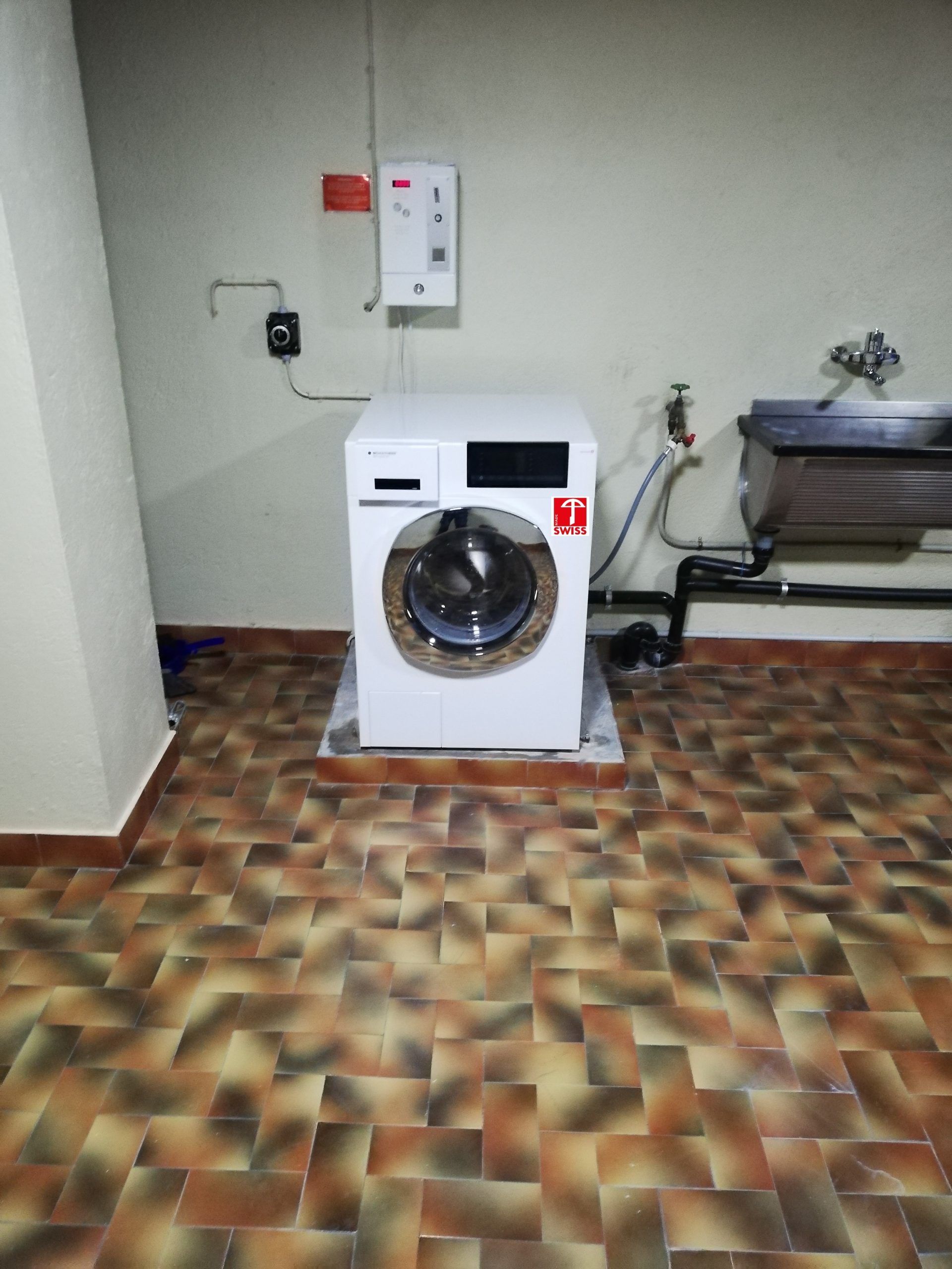 Machine à laver blanche sur un sol carrelé dans une buanderie, à côté d'un évier.