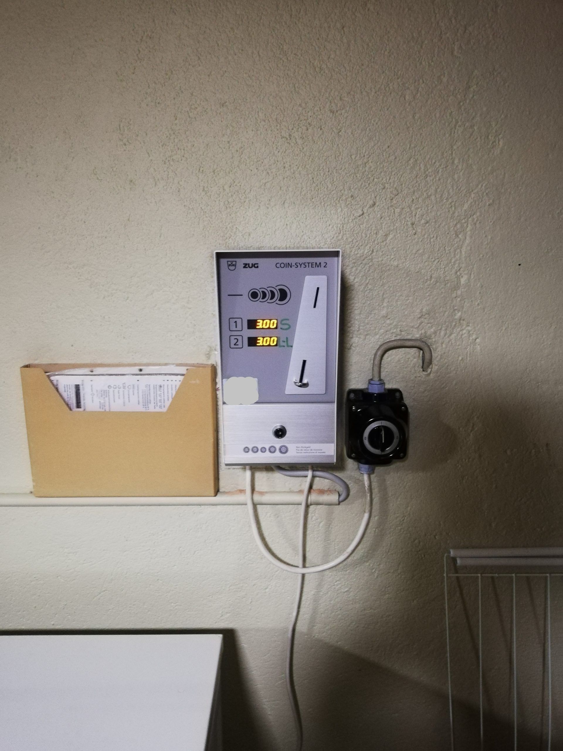 Un panneau de commande électronique mural avec un organiseur de papier à côté et une sortie d'eau en dessous.