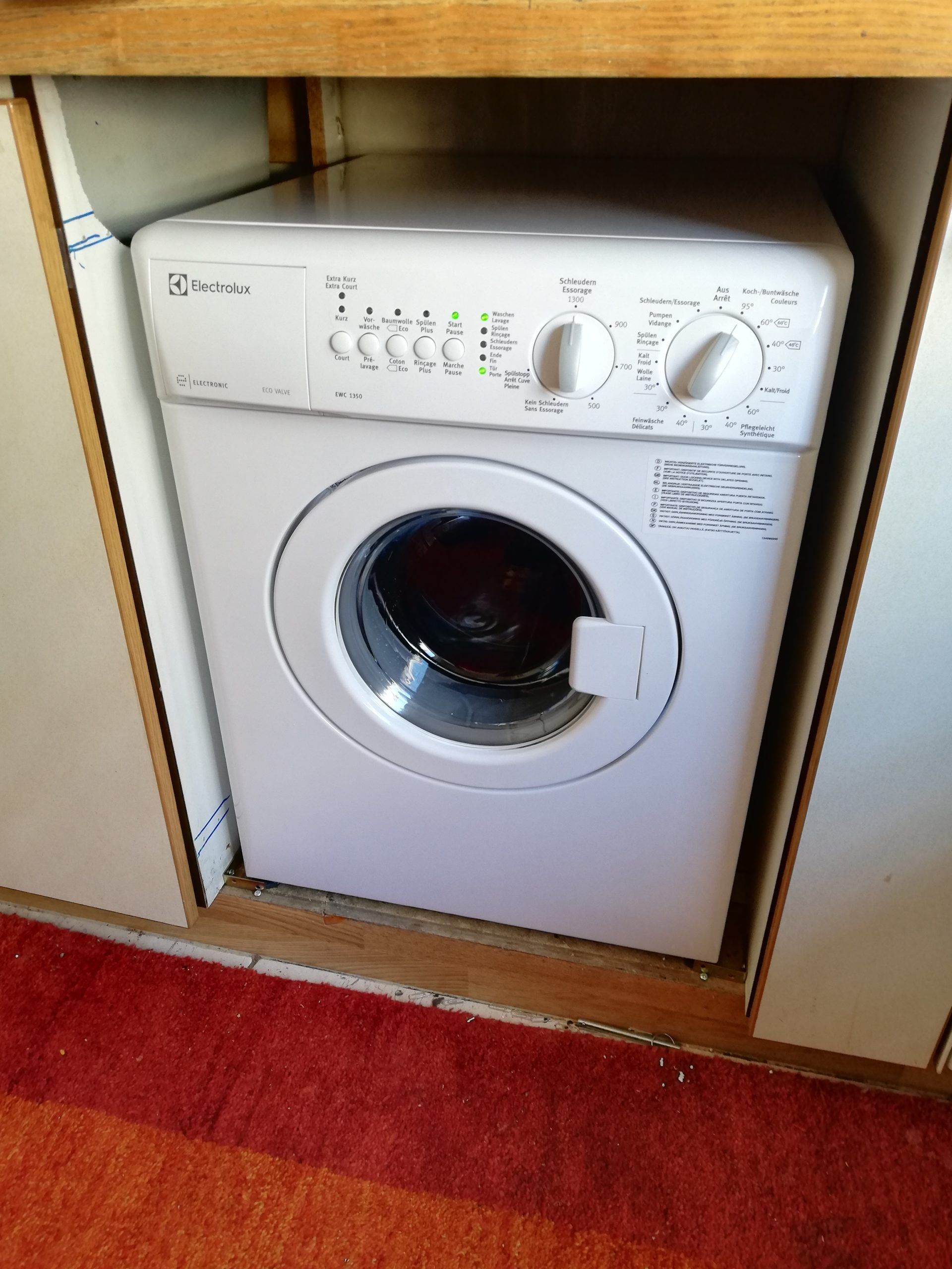 Machine à laver blanche à chargement frontal, encastrée entre des meubles blancs.