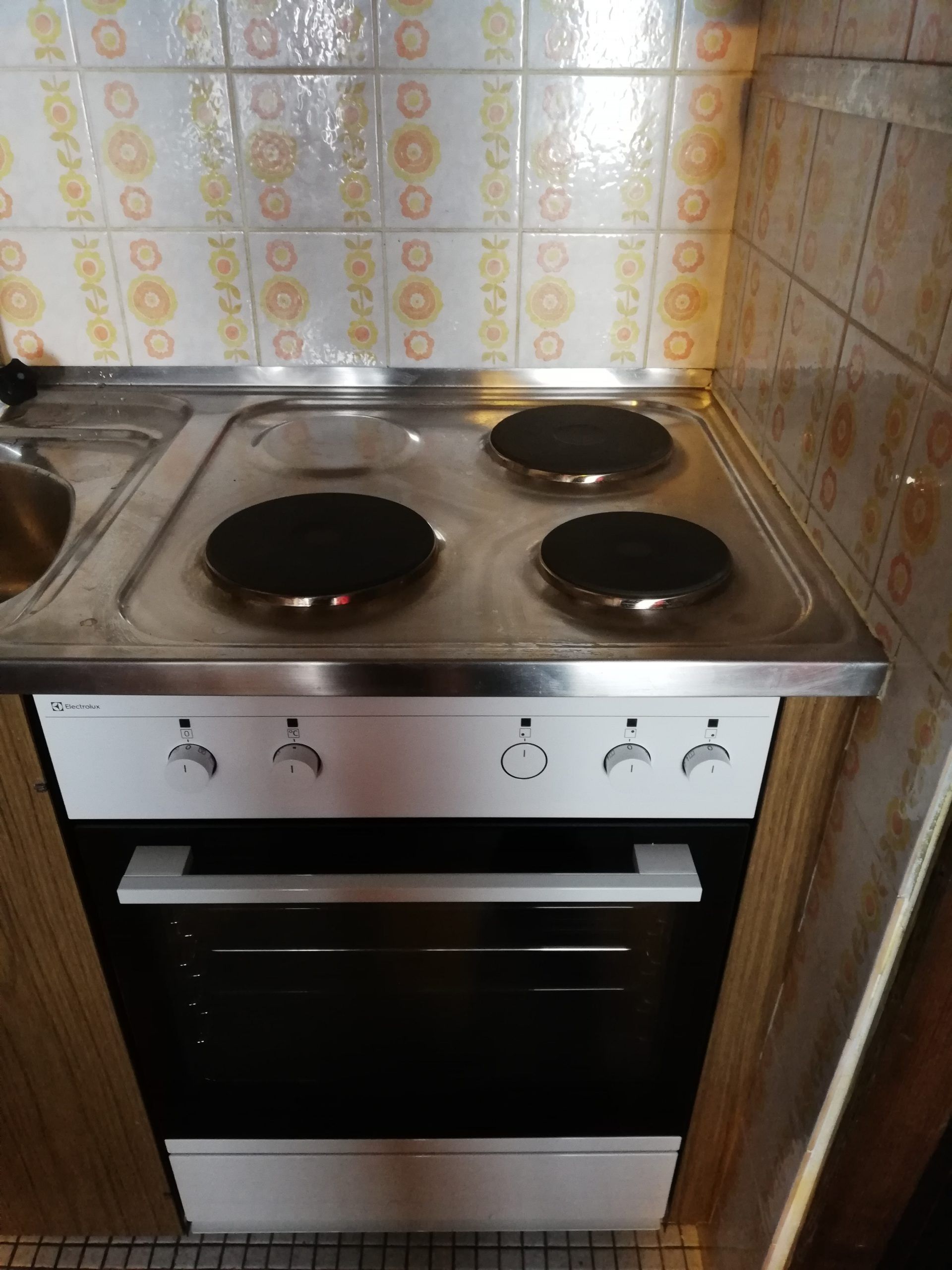 Plaque de cuisson électrique blanche à quatre brûleurs et four en dessous, boutons dans un contexte de cuisine.