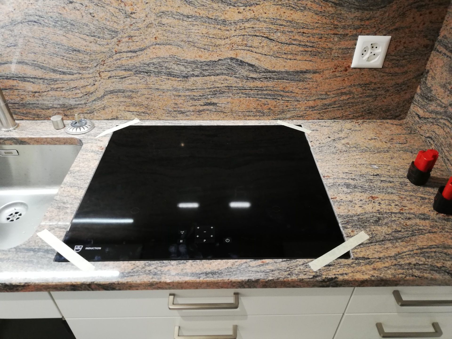 Plaque de cuisson en vitrocéramique noire sur un plan de travail en granit, avec un petit évier à gauche.