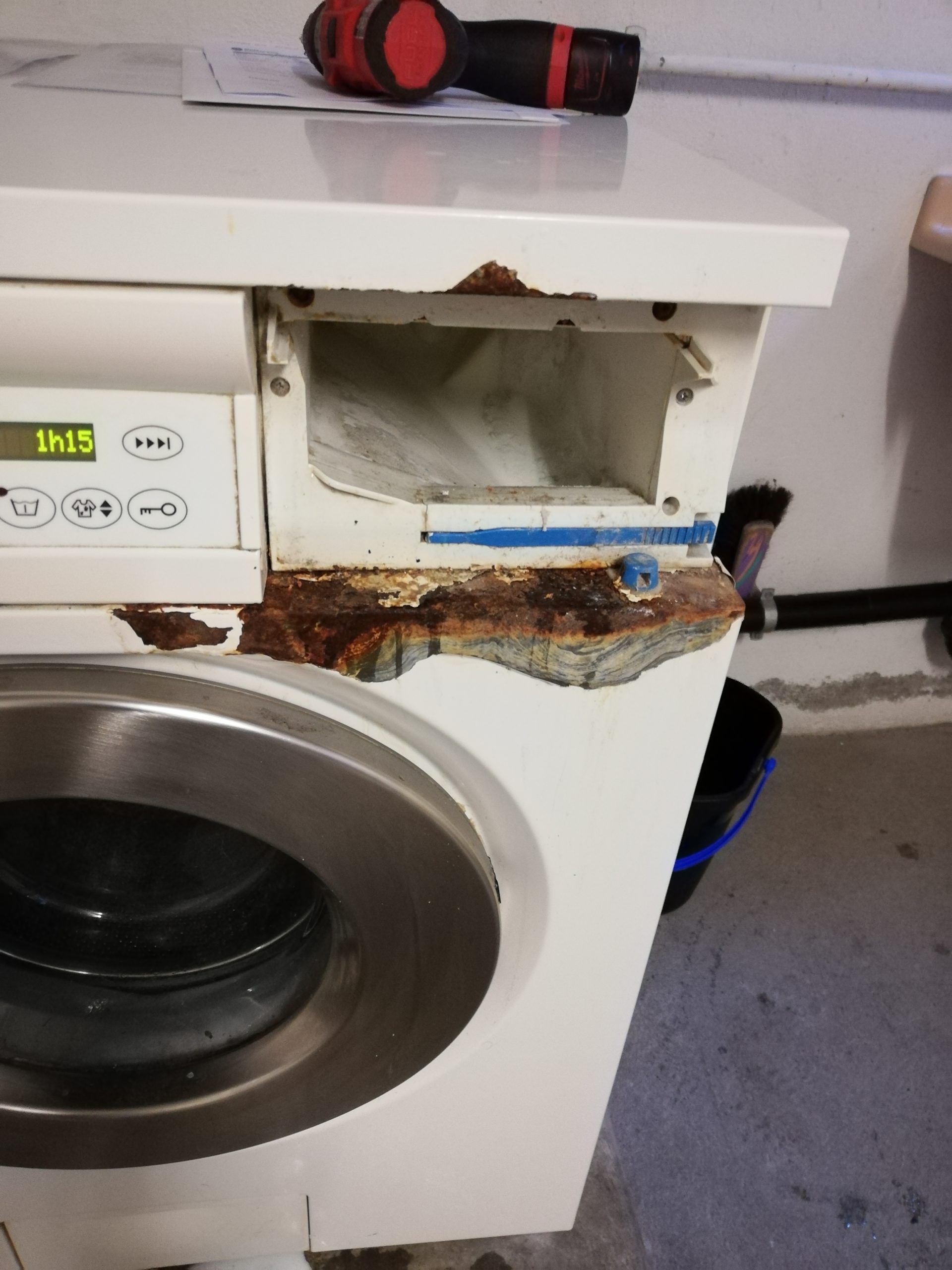 Une machine à laver présentant d'importants dégâts de rouille autour du bac à lessive.