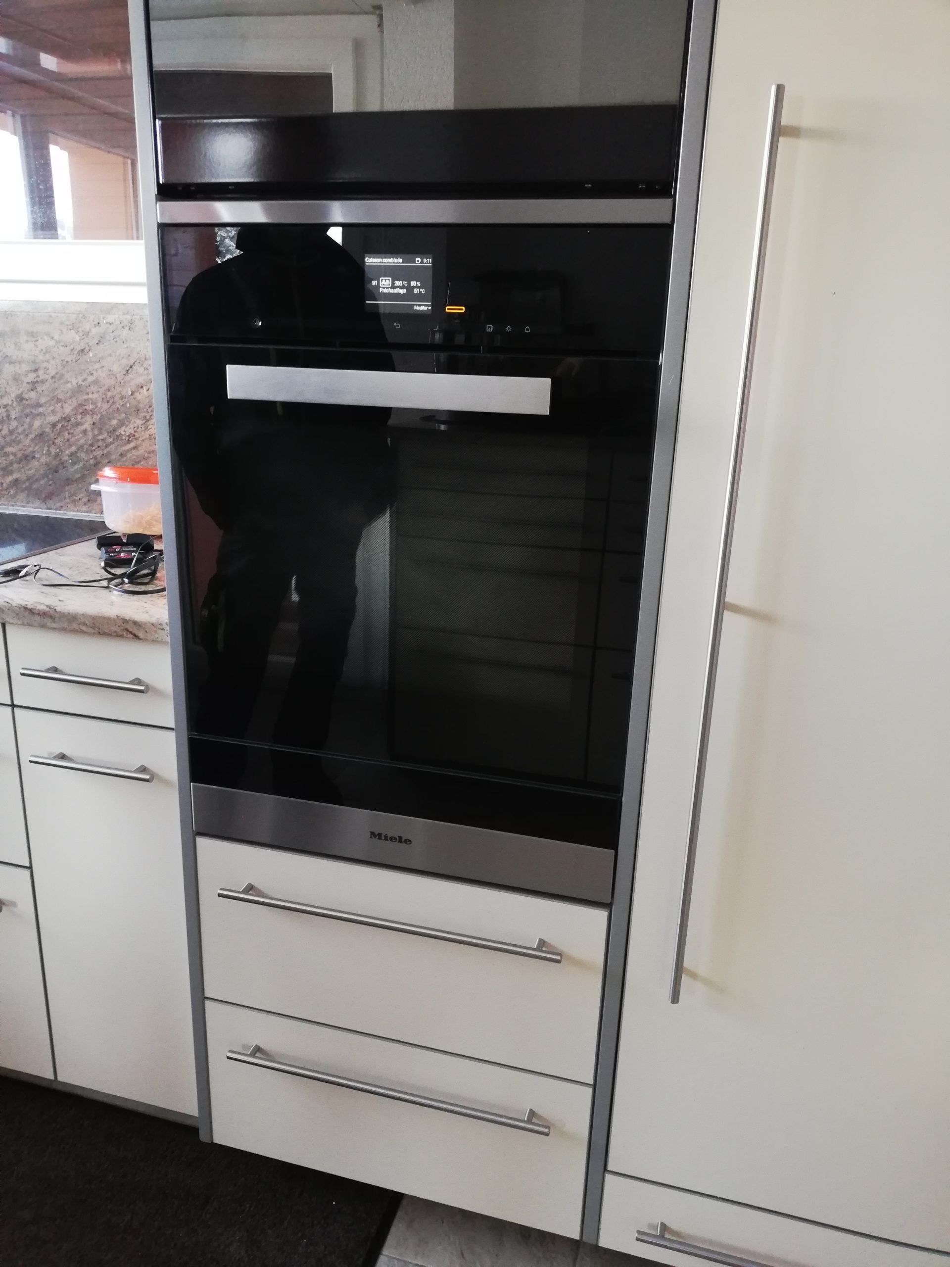 Four Miele encastré dans une cuisine. L'appareil est en acier inoxydable et noir, avec une poignée et un panneau de commande.