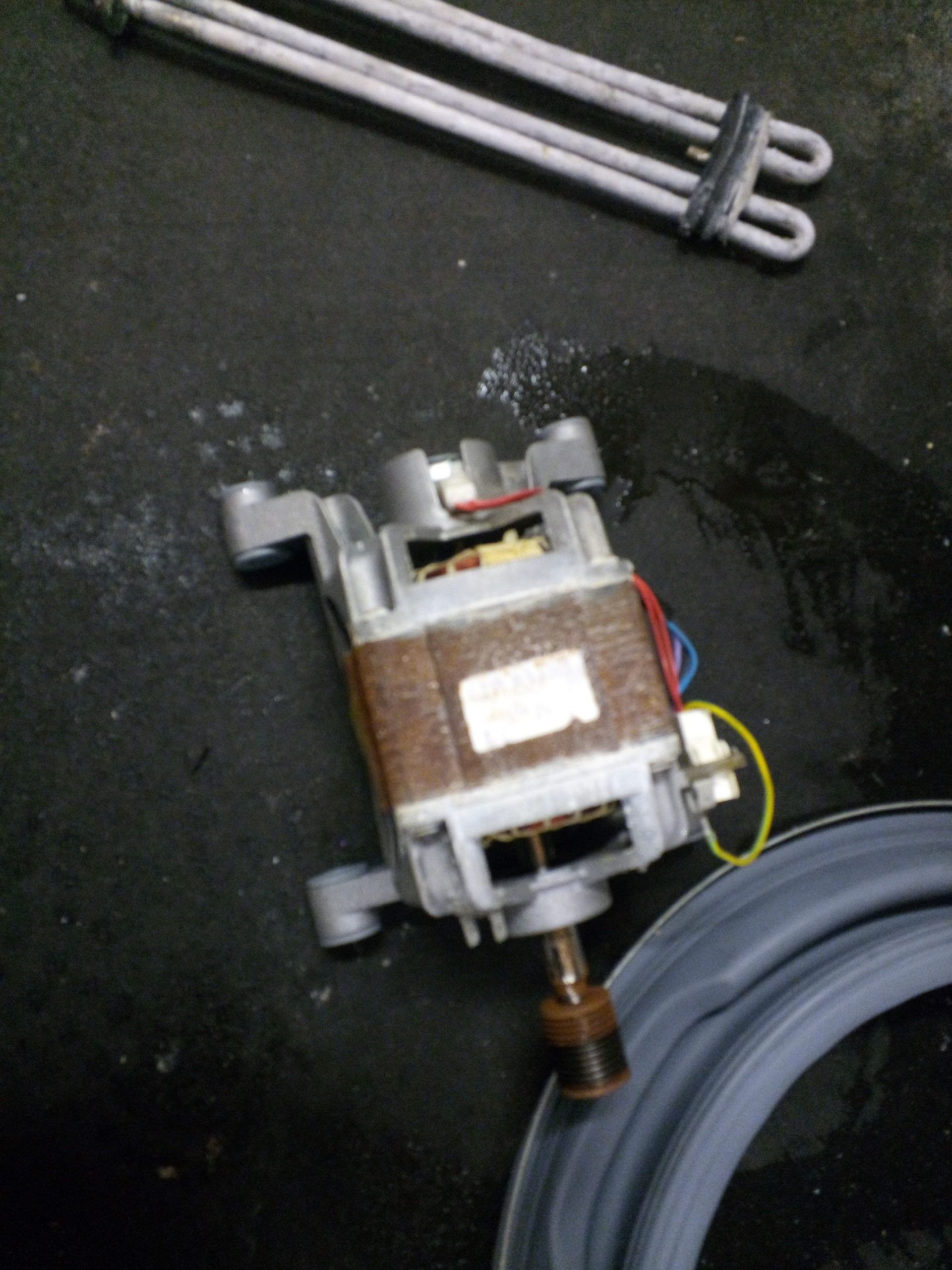 Moteur de machine à laver, gris métallisé avec bobine marron et fils colorés, sur une surface sombre.