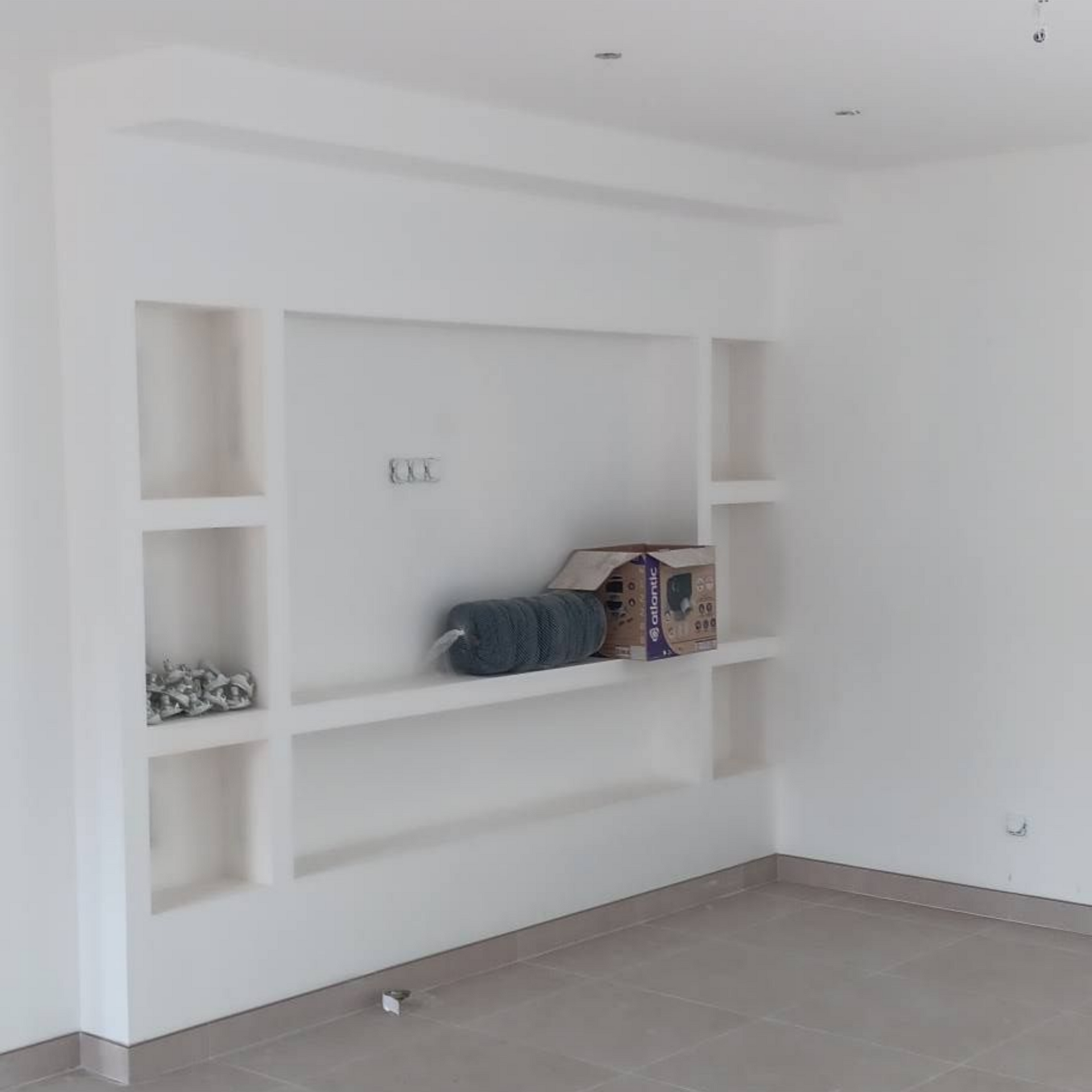 Meuble mural blanc vide avec étagères encastrées, sol gris.