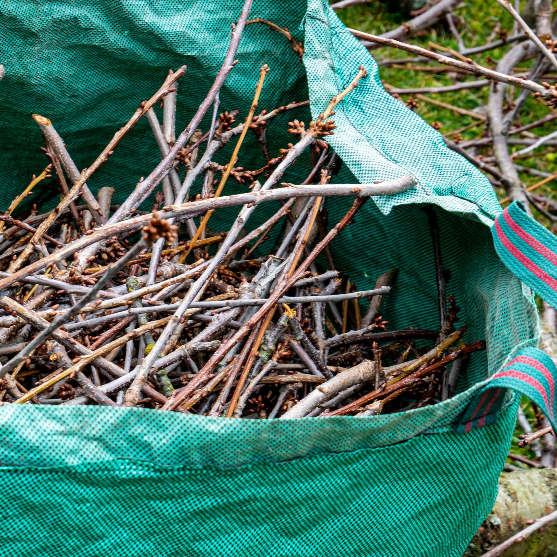 Sac vert rempli de brindilles et de branches brunes, à l'extérieur.