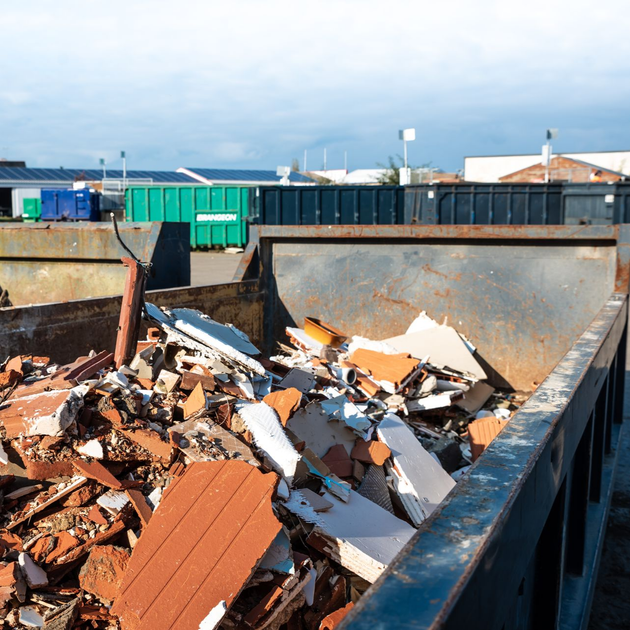 À l'extérieur, une benne à ordures remplie de débris de construction, notamment des briques et des plaques de plâtre.