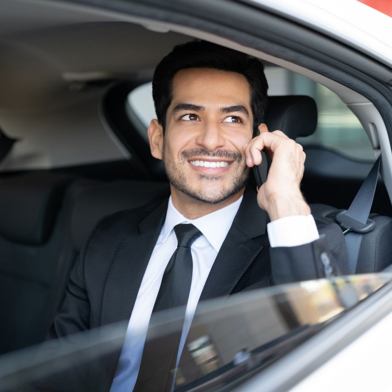 Un homme en costume sourit en téléphonant dans sa voiture.