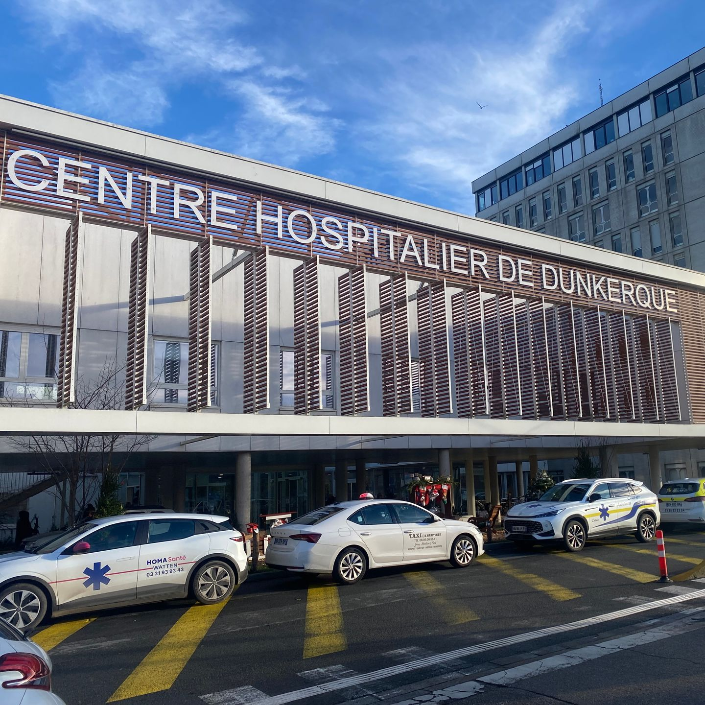 Hôpital de Dunkerque, voitures garées devant, dont des ambulances. Ciel bleu.