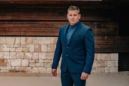 Un hombre con traje y corbata está parado frente a un muro de piedra.
