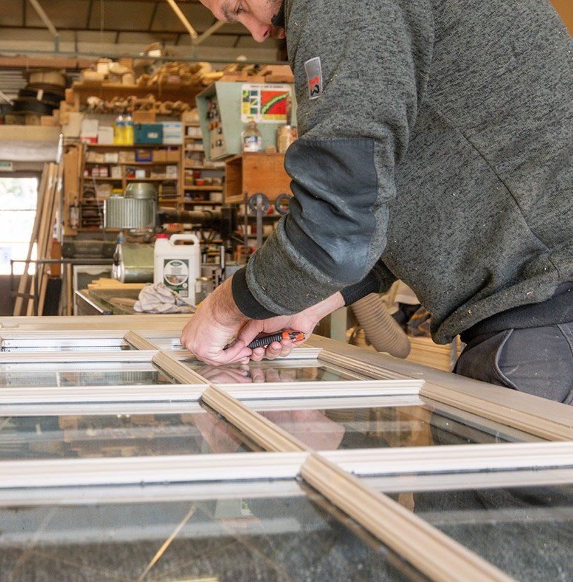 Menuisier travaillant sur une porte intérieure en bois de couleur blanche comportant des carreaux de verre