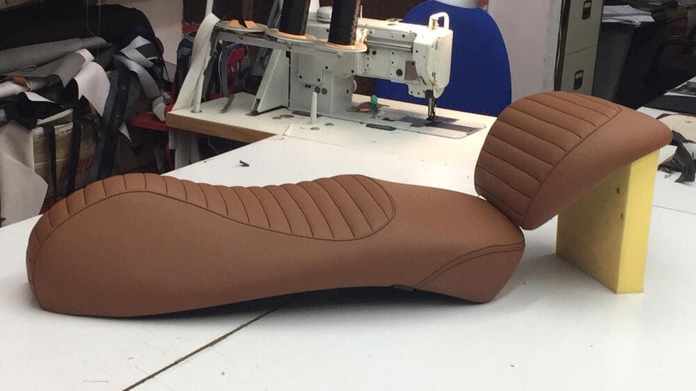 Un asiento de cuero marrón está sobre una mesa al lado de una máquina de coser.