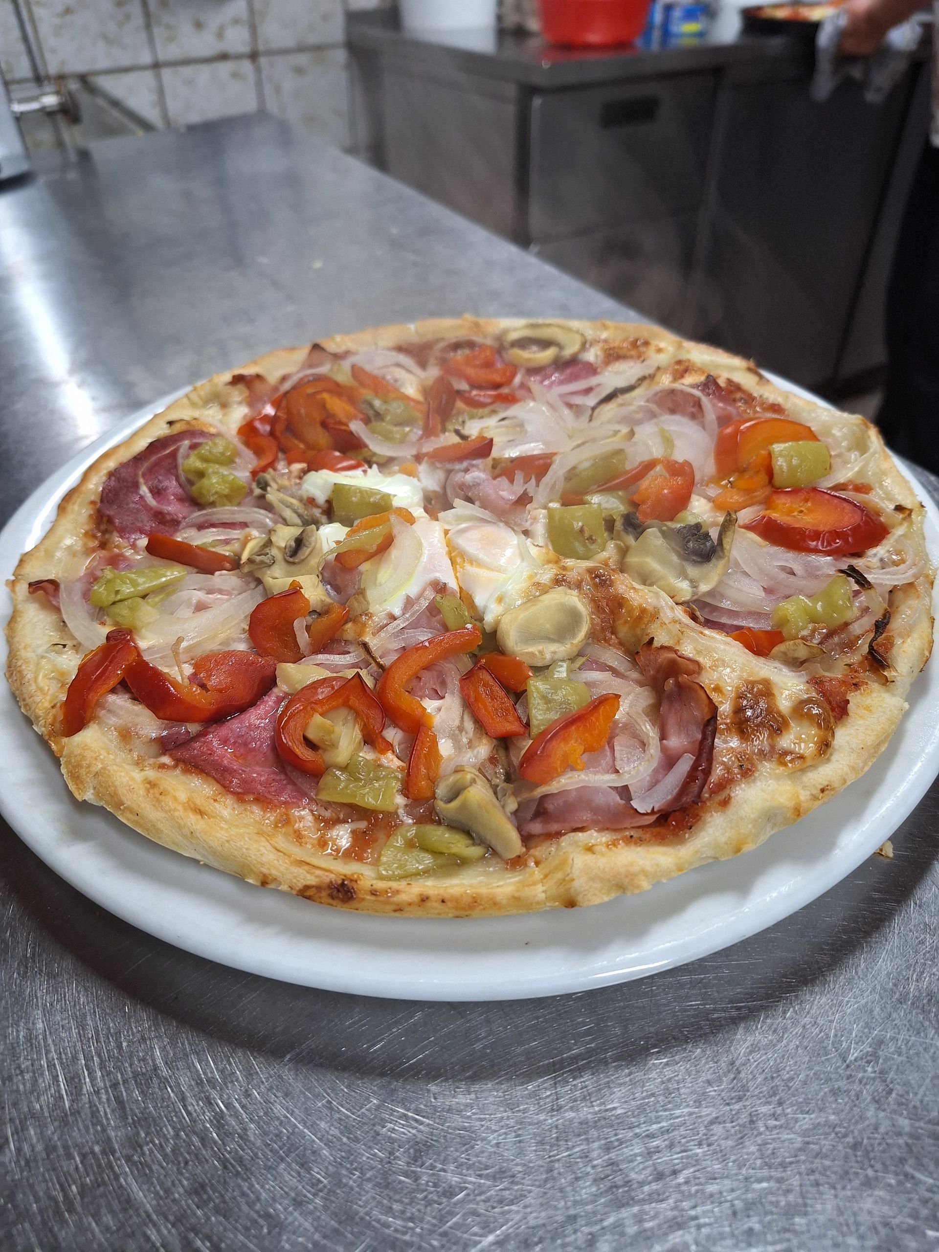 Pizza im Holzofen, die mit einem langen Pizzaschieber gewendet wird; der Ofeninnenraum ist warm beleuchtet.