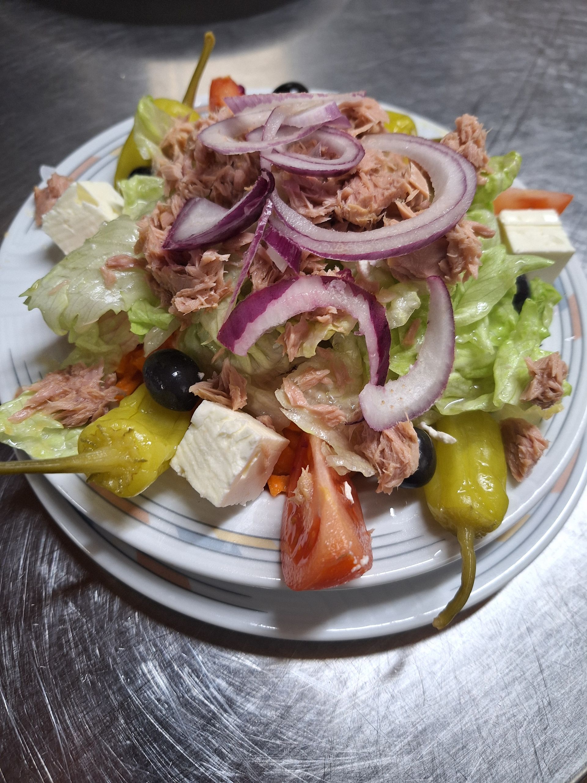 Salat aus gemischtem Grünzeug, Tomaten, Gurken und roten Zwiebeln auf einem weißen Teller; Draufsicht.