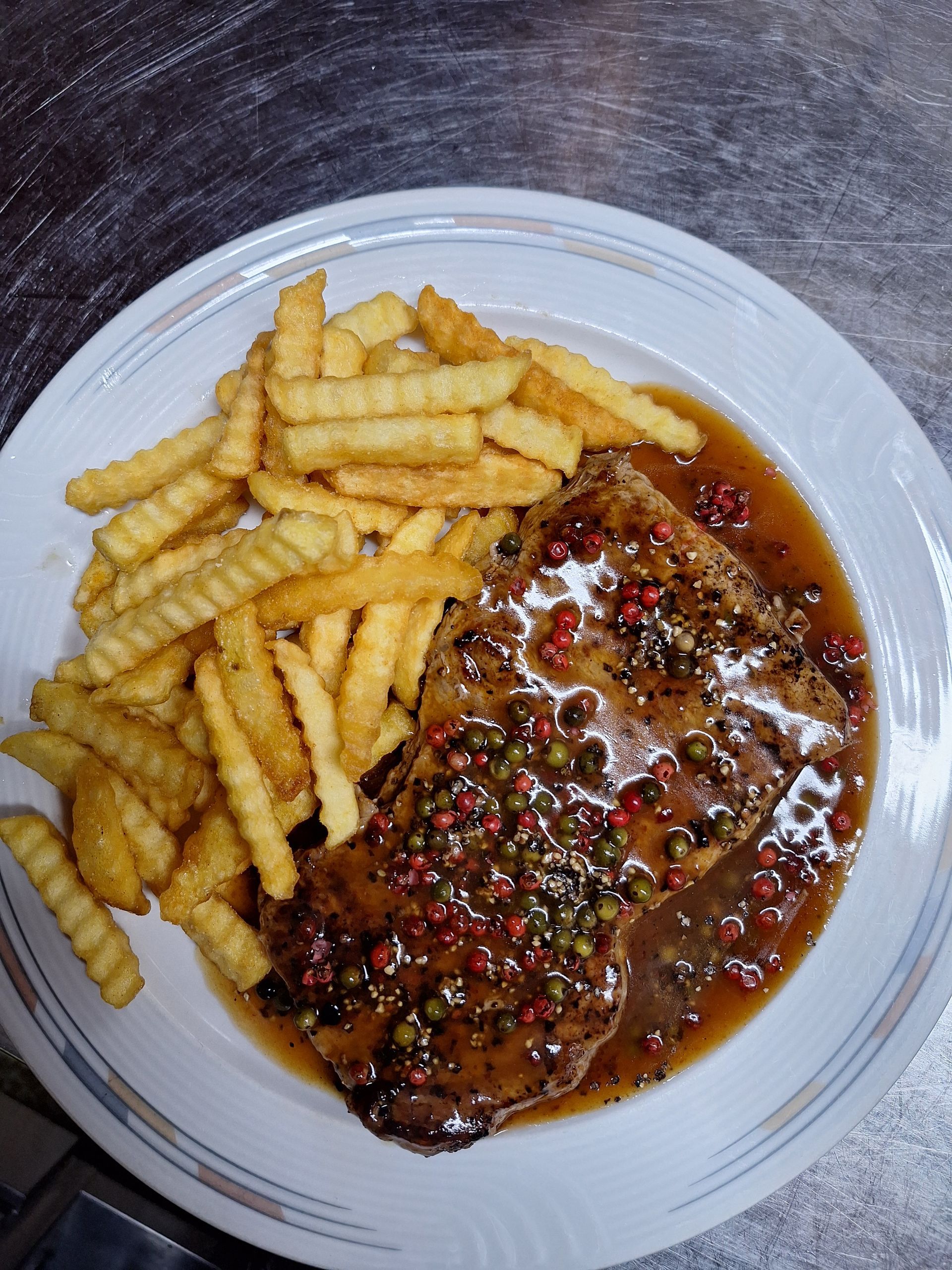 Gegrilltes Steak auf einem schwarzen Teller mit Petersilie und Silberbesteck; auf einer dunklen Oberfläche.