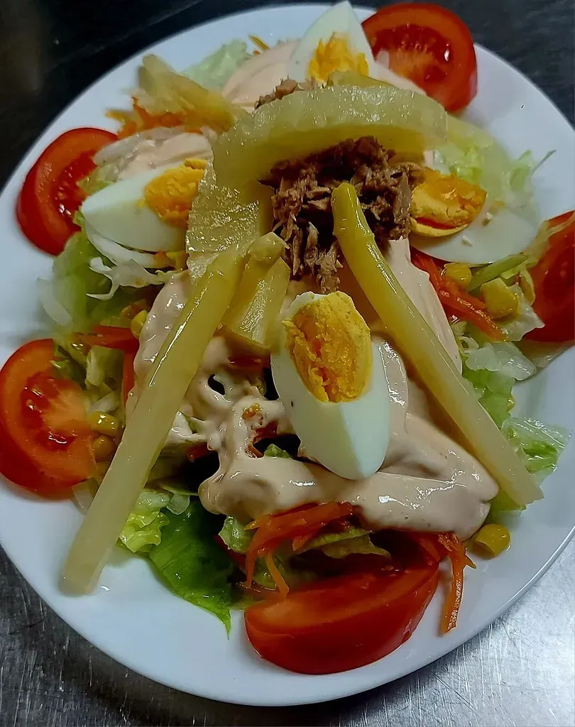 Una ensalada con atún, rodajas de huevo duro, tomates, piña y aderezo cremoso, servida en un plato ovalado blanco.