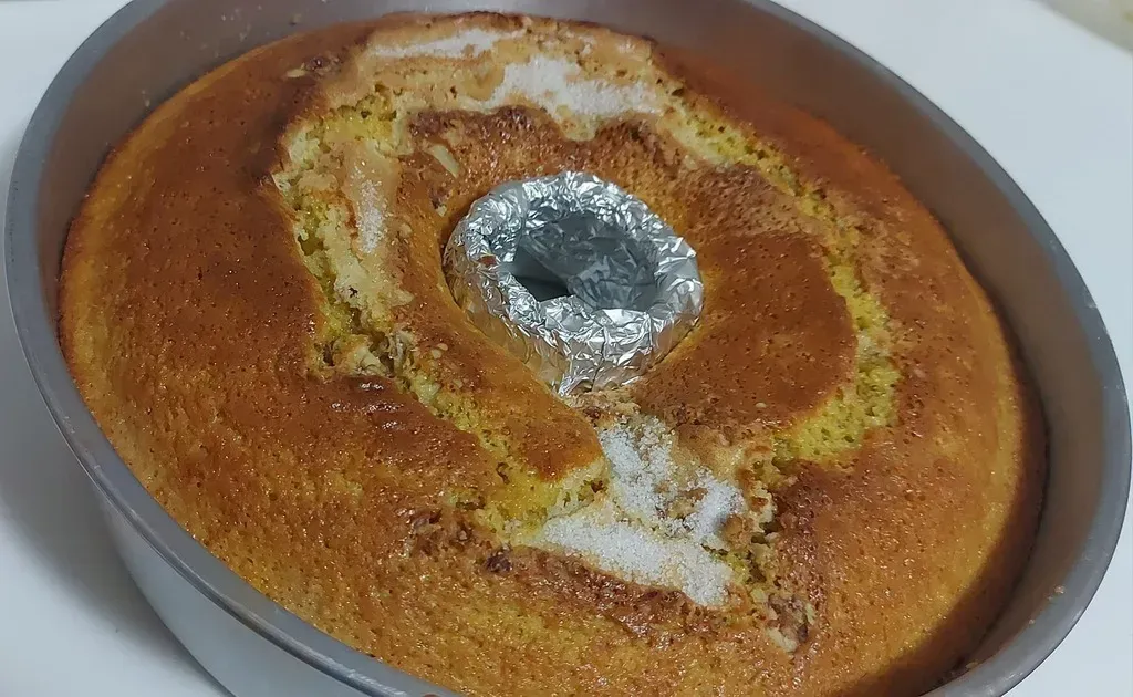 Un bizcocho en forma de anillo, recién horneado y de color marrón dorado, colocado en el centro de un molde redondo de metal, con un agujero en el medio cubierto con papel de aluminio.