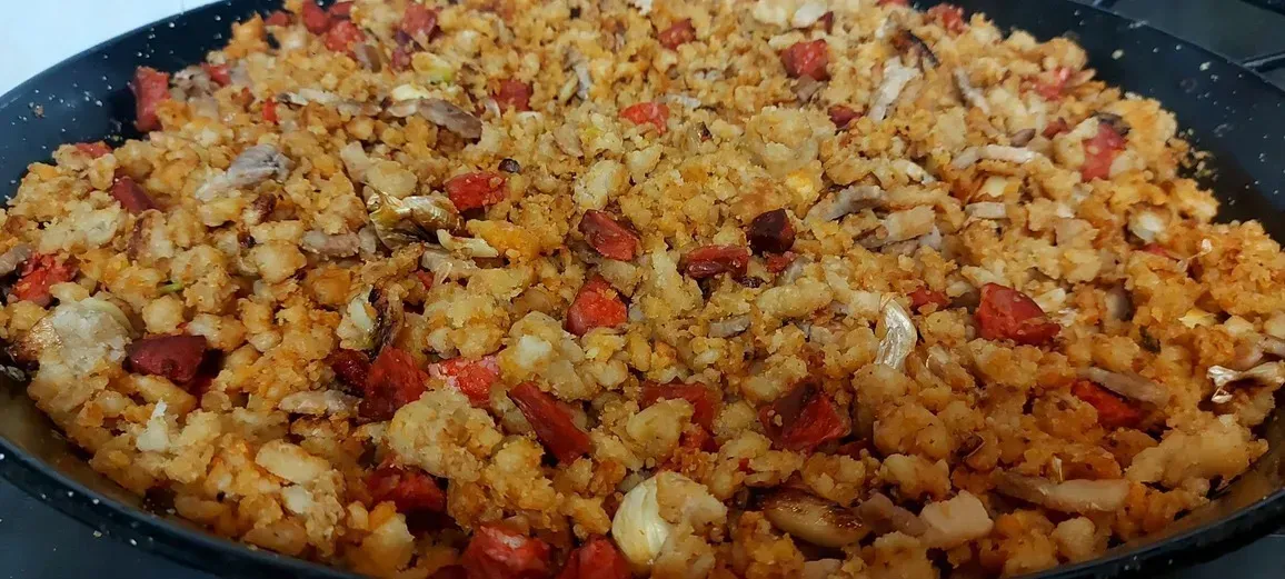 Primer plano de las migas, un plato español con pan rallado tostado, pimientos rojos, ajo y trocitos de salchicha, cocinado en una sartén.