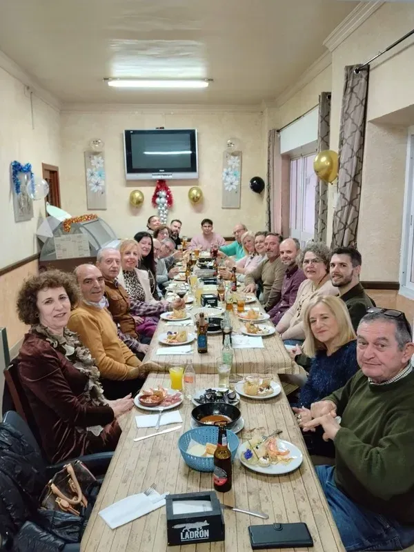 Un grupo de personas sentadas en una mesa larga, tipo banquete, en un comedor, compartiendo una comida y bebidas.