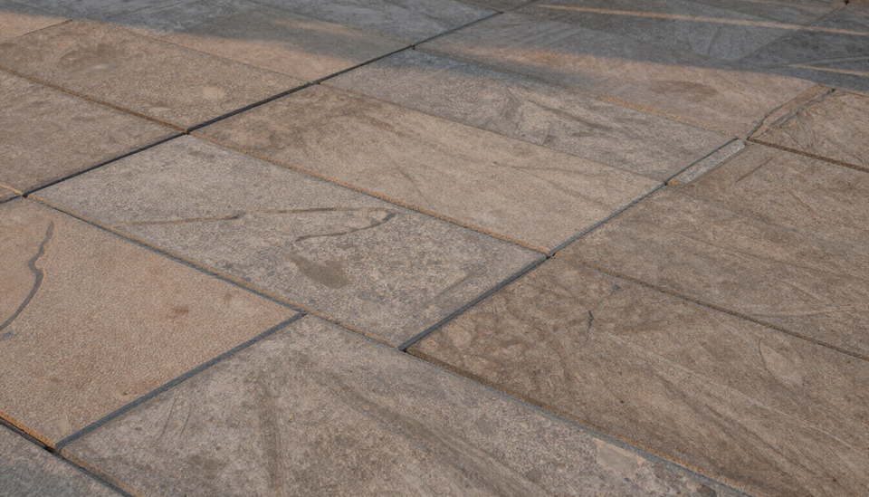 Primer plano de un pavimento de piedra de color beige y gris con grandes adoquines rectangulares y juntas visibles.