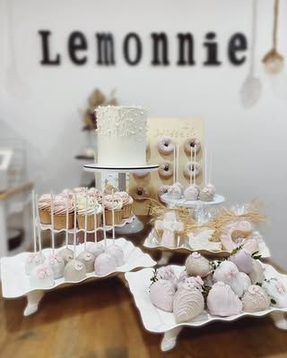 Mesa de postres con tartas, cake pops y pasteles sobre soportes blancos, bajo un letrero de “Lemonnie”