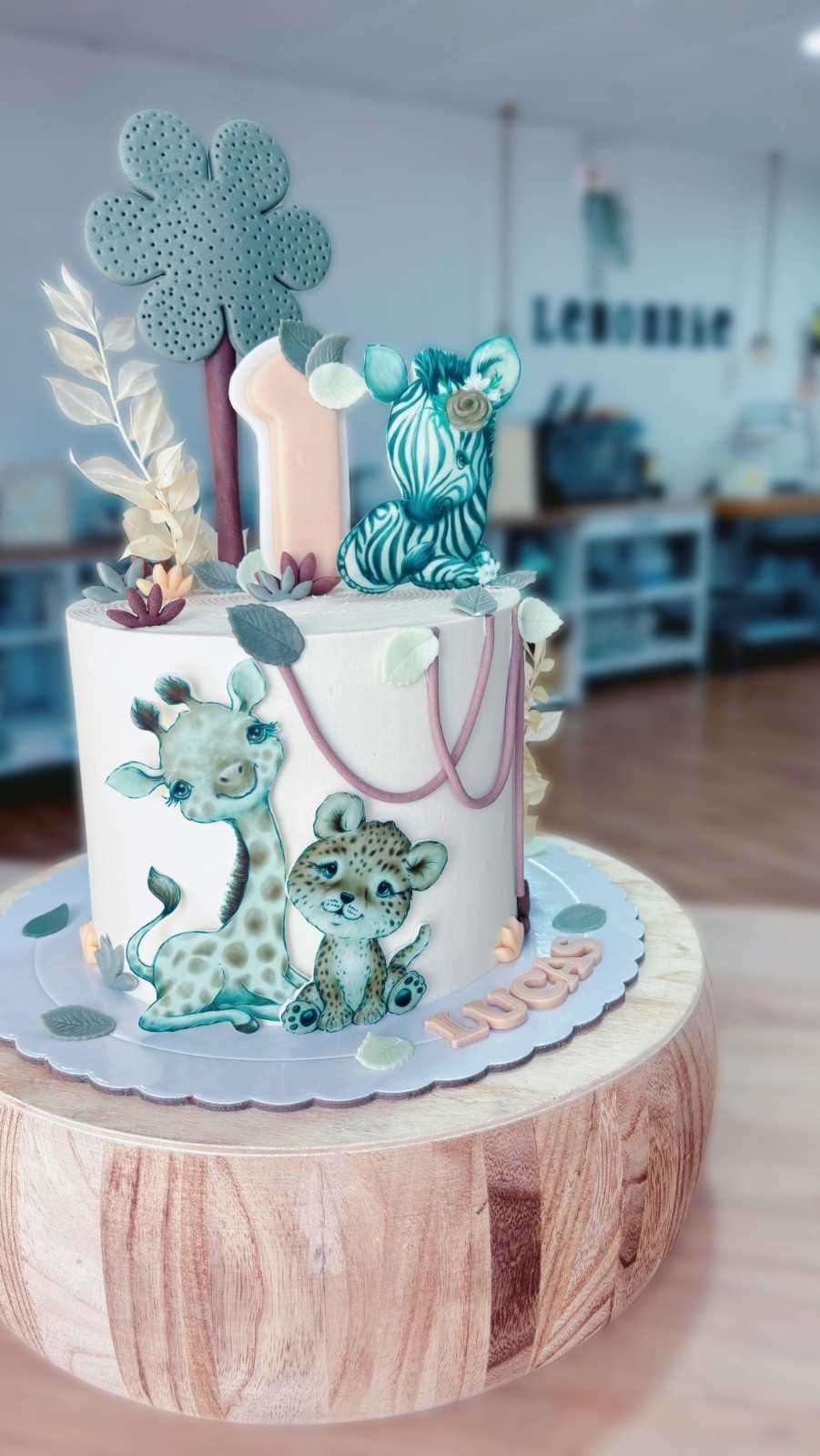 Tarta decorada en azul y blanco, con flores, una vela y figuritas, sobre un soporte de madera