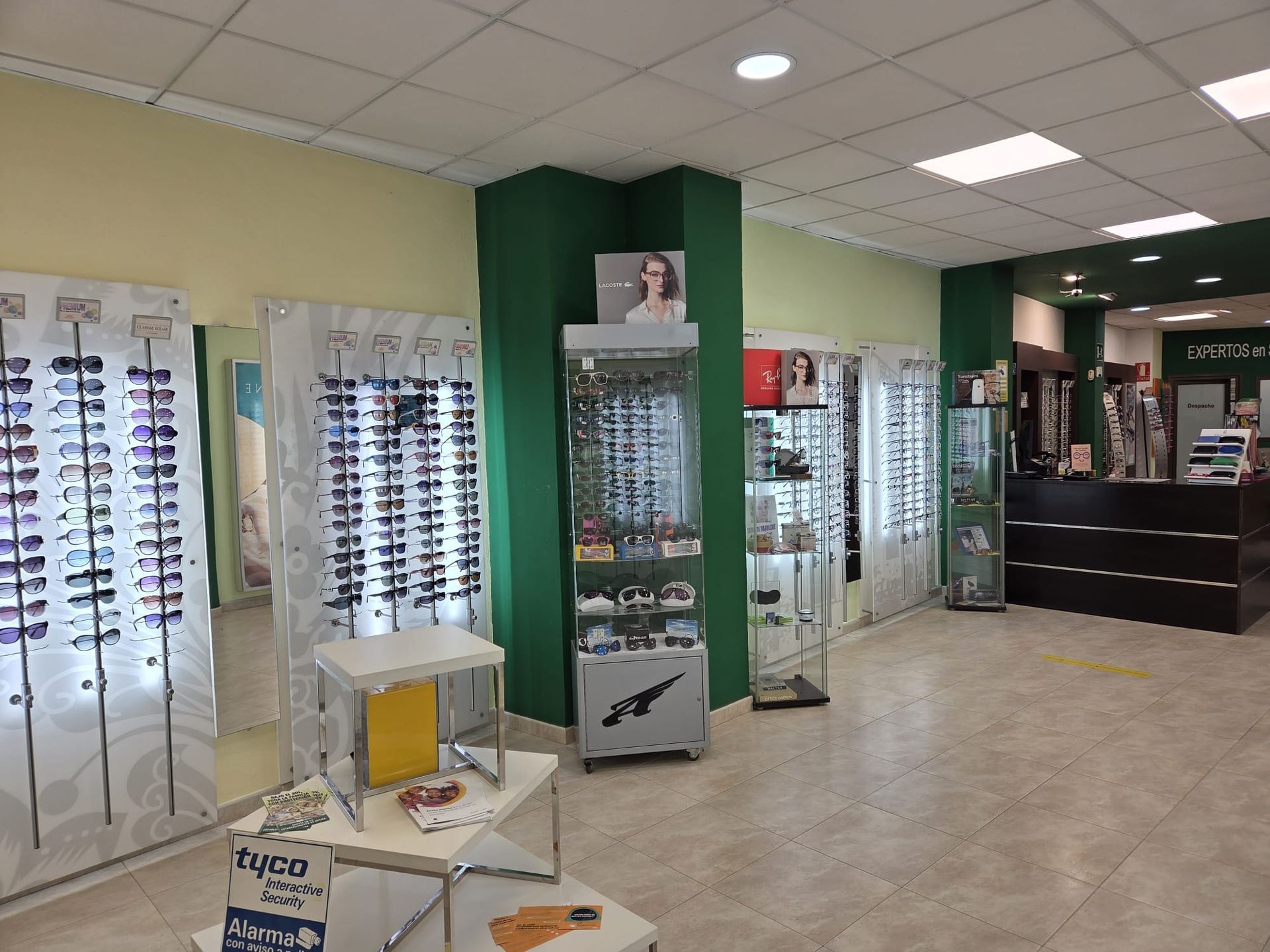 Interior de una óptica con la imagen de un bebé y expositores de gafas. Decoración en verde y blanco.