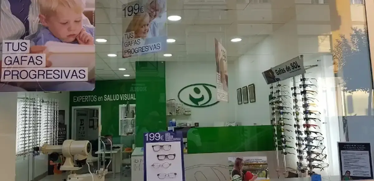 Interior de una óptica con la imagen de un bebé y expositores de gafas. Decoración en verde y blanco.