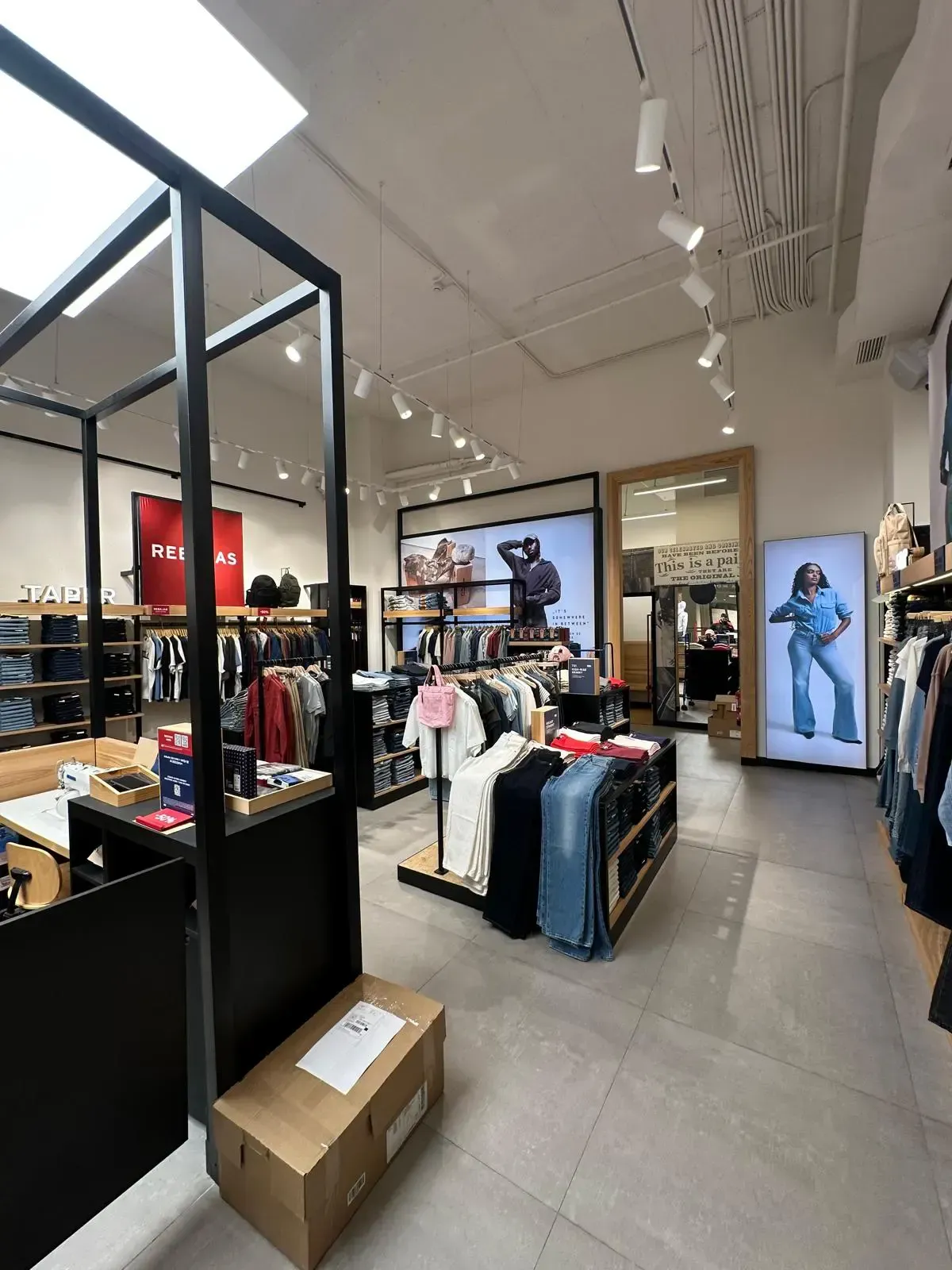 Interior de una tienda de ropa con percheros, una caja grande y una iluminación brillante en el techo.