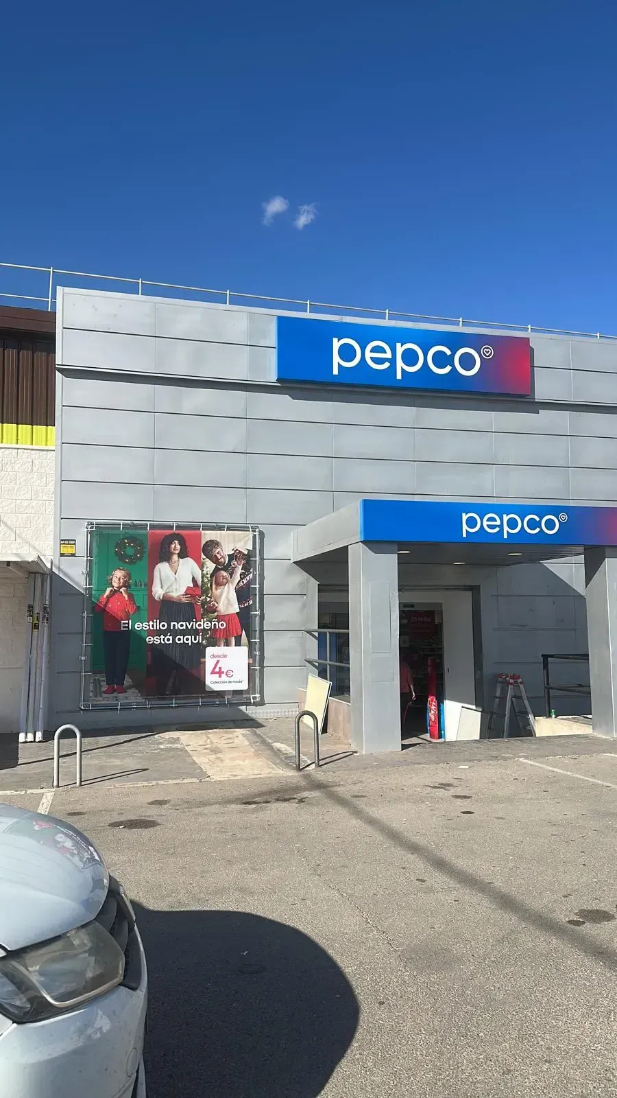 Exterior de la tienda Pepco bajo un cielo azul, con señalización y exhibición publicitaria.