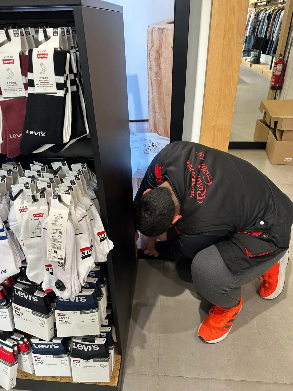 Una persona agachada, mirando hacia abajo, cerca de un escaparate de calcetines. 
