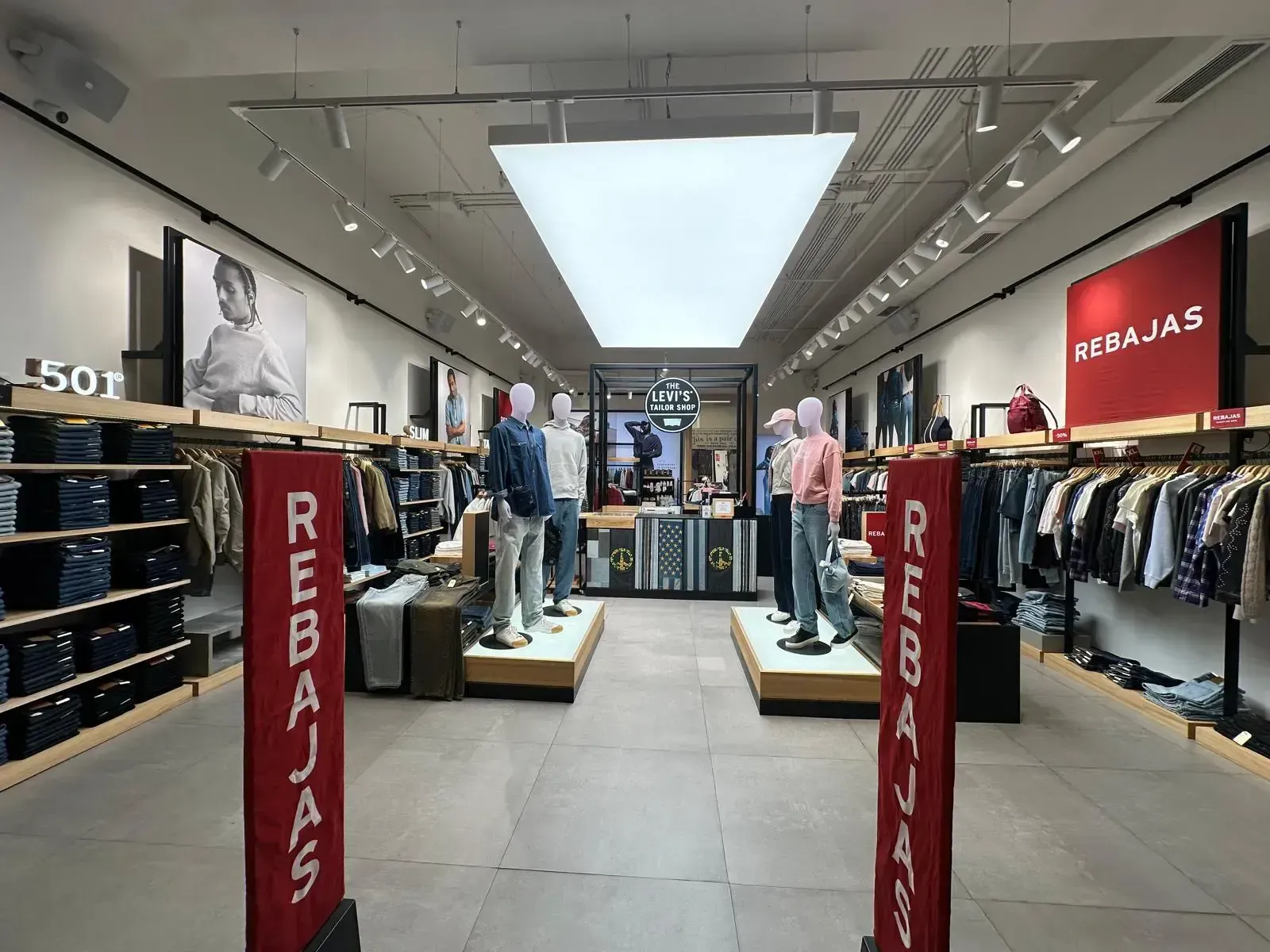 Dentro de una tienda de ropa, con maniquíes, estantes de ropa y carteles de venta.