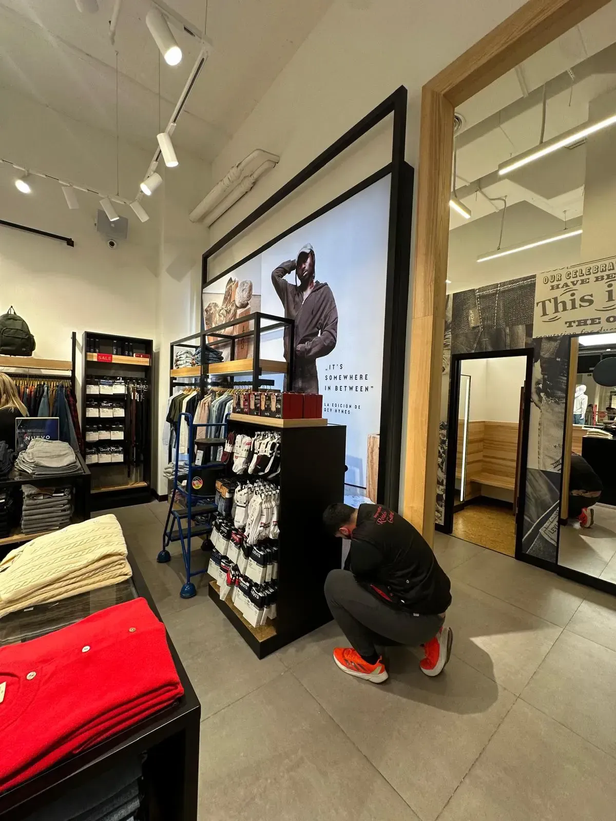 Un hombre ajusta la mercancía en una tienda de ropa. Interior de la tienda con estantes, ropa y publicidad.