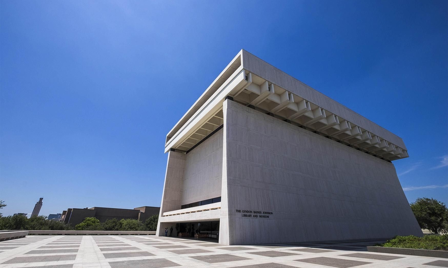 John F. Kennedy Center for the Performing Arts, Washington, D.C. Large white building with square top and open space at the front. Blue sky.