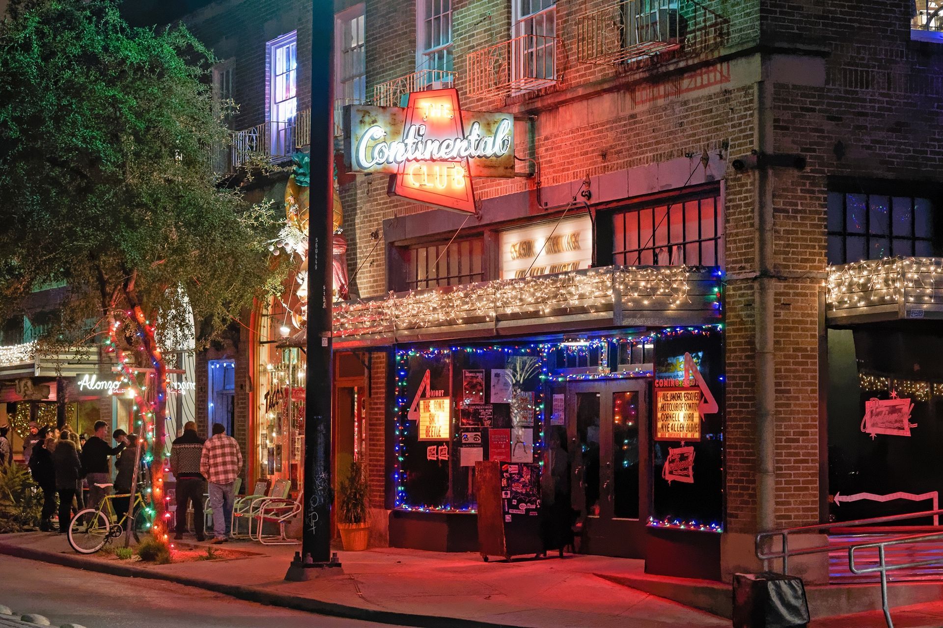 Exterior of a bar at night, lit with red and blue lights. A neon sign reads