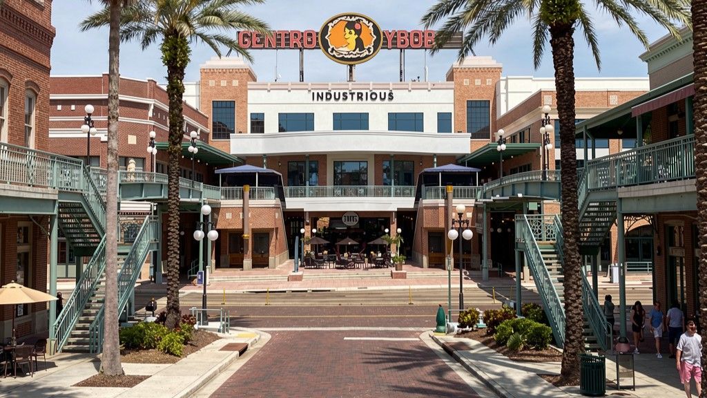 An outdoor view of the brick-paved Ybor City plaza in Tampa, featuring palm trees, stairs, and historic buildings.