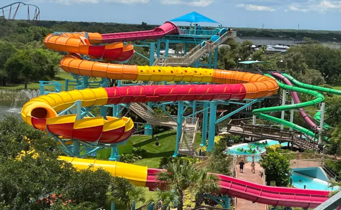 Colorful water slides winding down a tower at a water park. Bright tubes and a pool area.