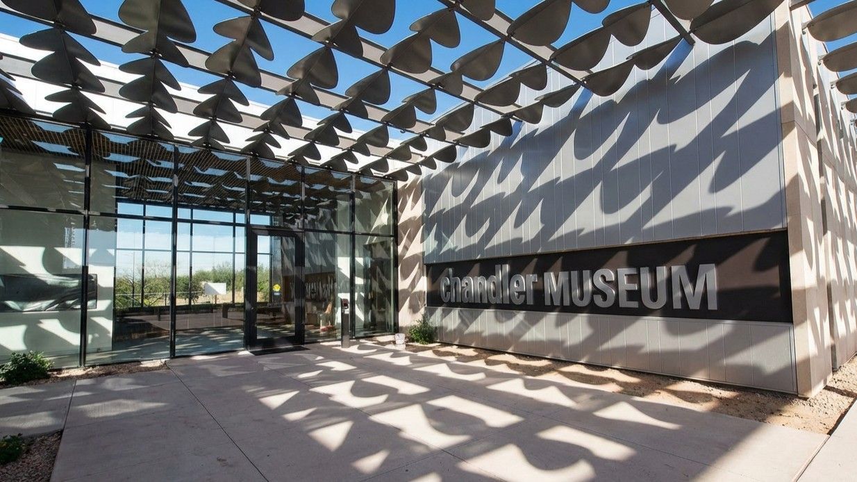 Entrance to the Chandler Museum featuring a patterned overhead shade structure casting shadows on the building wall.