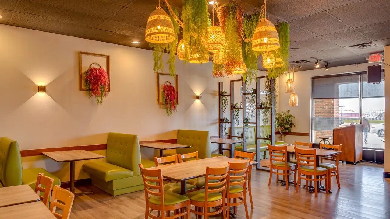 Restaurant interior with tables, booths, and hanging wicker lamps, with floral wall art.