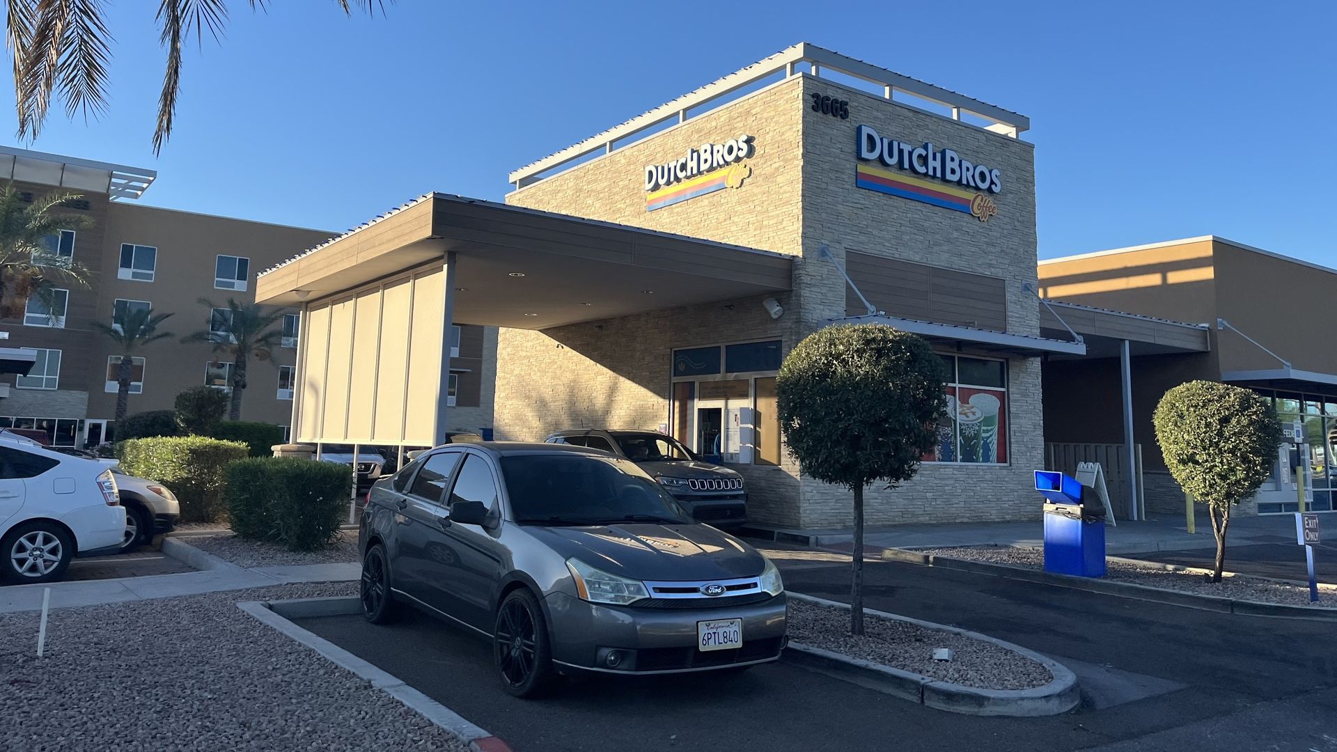 Exterior of a tan bank building with a drive-up lane and a canopy; cars parked in front.
